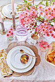 Gedeckter Frühstückstisch mit rosa Blütenarrangement und frischem Gebäck
