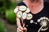 Frau hält Kräuterstecker für Estragon, Thymian und Petersilie in der Hand