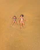 Aerial view of two girls having fun lying on the beach in Cajueiro, Brazil.