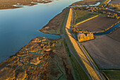 Luftaufnahme eines kleinen Dorfes, das von landwirtschaftlichen Flächen umgeben ist, während eines malerischen Sonnenuntergangs, Niederlande.