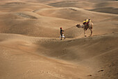 Luftaufnahme eines Mannes mit Kamel, der zügig auf den Sanddünen von Khuri, Jaisalmer, Rajasthan, Indien läuft