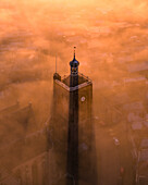 Aerial view of a mystical cityscape with a church tower emerging from fog and low clouds at sunrise, Workum, Friesland, Netherlands.