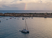 Aerial view of ancient castle ruins and serene sea with boats under a rainbow, Methoni, Greece.