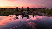 Luftaufnahme eines ruhigen Sees bei Sonnenuntergang mit Reflektionen und einem Wohnmobil, Odivelas, Portugal.