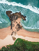 Aerial view of girl lying on rocky private beach by the ocean with waves crashing in Bentota, Sri Lanka