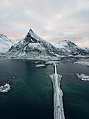 Aerial view of car driving over famous Fredvang Bridges and snowy mountains, Lofoten Islands, Northern Norway in the Arctic Circle