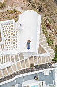 Aerial view woman lying on the roof on Santorini traditional house with surrounding staircase, Greece.