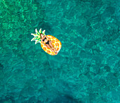Aerial view of woman floating in inflatable pineapple on Atokos island, Greece.