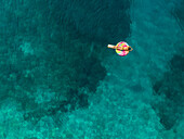 Aerial view of woman floating on inflatable lollipop mattress on Atokos island, Greece.
