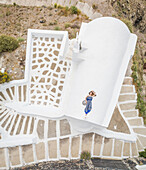 Aerial view woman lying on the roof on Santorini traditional house with surrounding staircase, Greece.