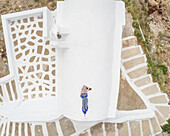Aerial view woman lying on the roof on Santorini traditional house with surrounding staircase, Greece.