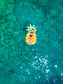 Aerial view of woman floating in inflatable pineapple on Atokos island, Greece.