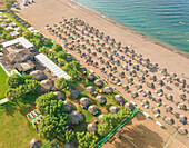 Luftaufnahme eines Strandes mit Reihen von Strohsonnenschirmen in einem Ferienort, Achaia, Griechenland.