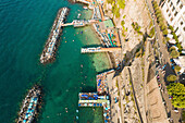 Aerial view of beautiful coastline with rocky cliffs, pier, and people enjoying the beach, Sorreto, Italy.