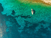 Aerial view of single sailboat anchored close to the shore in the mediterranean sea, Ithaki island, Greece.