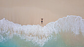 Top aerial view of a man lying on sand at diamond beach on a bright fine day in Nusa Penida Island, Indonesia.