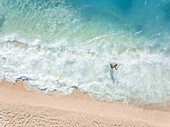 NIKITAS, GREECE - 13 JULY 2018: Aerial view of kid playing in waves on sandy beach in turquoise sea.