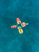 Aerial view of women in bikinis holding hands on inflatable mattresses on Atokos island, Greece.