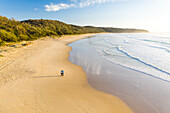 Aerial view of couple walking at Alexandria beach during sunset, Noosa, Australia.