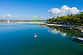 Aerial view of a blonde girl paddling a surfboard along the coast, Pointe de Flacq, Mauritius.