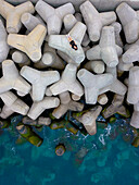 Luftaufnahme eines ruhigen Wellenbrechers mit einer Frau, die sich am schönen blauen Meer sonnt, Funchal, Portugal.