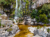 Aerial view of a woman standing in front of a waterfall in black swimsuit, Rawsonville, Western Cape, South Africa.