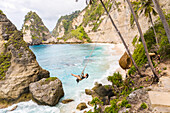Aerial view of attractive woman swinging at Diamond Beach shore, Indonesia.
