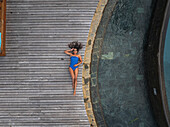 Aerial view of beautiful woman sunbathing on a private wooden deck by the pool at Anahita hotel, Flacq, Mauritius.