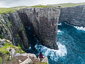 Aerial view of woman standing on the edge of tourists English Slave cliff, Faroe island.