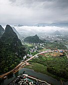 Aerial view of beautiful karst mountains and a tranquil river winding through a lush valley with a picturesque village, Guilin, China.