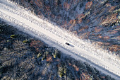 Aerial view of a blue car driving in the snowy forest in Estonia.