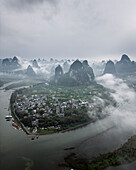 Aerial view of picturesque karst mountains and a serene river with a remote village shrouded in fog, Guilin, China.