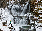 Aerial view of crowley waterfall with a woman standing on a rock in a snowy landscape, Unalaska, United States.