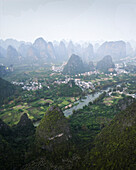 Aerial view of picturesque karst mountains and a serene river winding through a lush valley with a rural village, Guilin, China.