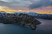 Aerial view of a mountain range with snow on the crests along the Dutch Harbour on Amaknak Island at sunset, Unalaska, Alaska, United States.
