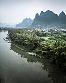 Aerial view of serene landscape with lush greenery, tranquil river, and rural village surrounded by mountains, Guilin, China.