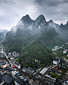 Aerial view of dramatic karst mountains and serene town enveloped in fog, Guilin, China.