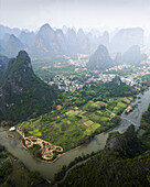 Aerial view of picturesque karst mountains and serene river winding through lush green fields and rural village, Guilin, China.