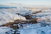 Luftaufnahme eines geothermischen Dampftopfs und eines geothermischen Kraftwerks im Hintergrund, dazwischen sind Seen mit blauem Wasser zu sehen, das von der Anlage abgelassen wird, Gunnuhver, Reykjanes-Halbinsel, Island
