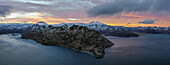 Panoramic aerial view of a mountain range with snow on the crests along the Dutch Harbour on Amaknak Island at sunset, Unalaska, Alaska, United States.