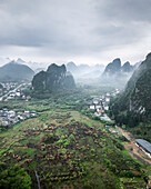Aerial view of picturesque karst mountains and a tranquil valley with a quaint village surrounded by lush greenery and mist, Guilin, China.