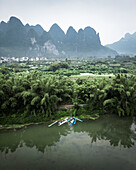 Aerial view of serene karst mountains and tranquil river surrounded by lush bamboo and greenery, Guilin, China.