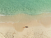 Luftaufnahme einer Frau, die sich an einem schönen Strand mit türkisfarbenem, klarem Wasser und weichem Sand entspannt, North Eleuthera, Bahamas