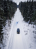Aerial view of a man lighting a blue smoke grenade on a snowy road in the forest in Estonia.