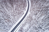 Aerial view of an empty road in the middle of the forest in winter in Estonia.
