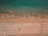 Aerial view of a girl in hat sitting on the beach, Comporta, Setubal district, Portugal. A girl is watching on the turquoise ocean and dreaming