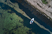 Aerial view of two people in a small boat moored close to a sandy beach in Estonia.