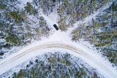 Aerial view of a car driving in the snow in the forest of Estonia.