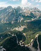 Aerial view of majestic mountains and a winding road amidst a picturesque forest and serene valley, Malesi e Madhe, Albania.