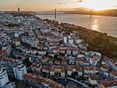 Aerial view of Cacilhas little township along the Tagus river at sunset with April 25th bridge and Cristo Rei statue in background, Almada, Portugal.